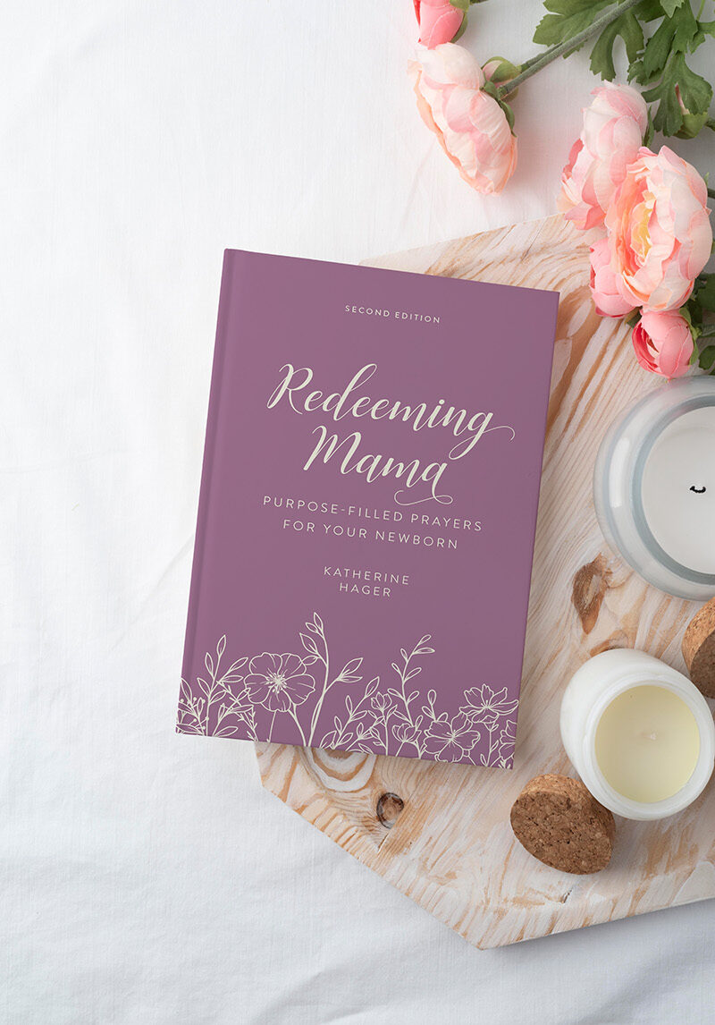 Devotional "Redeeming Mama" by Katherine Hager on a wooden tray with candles and florals