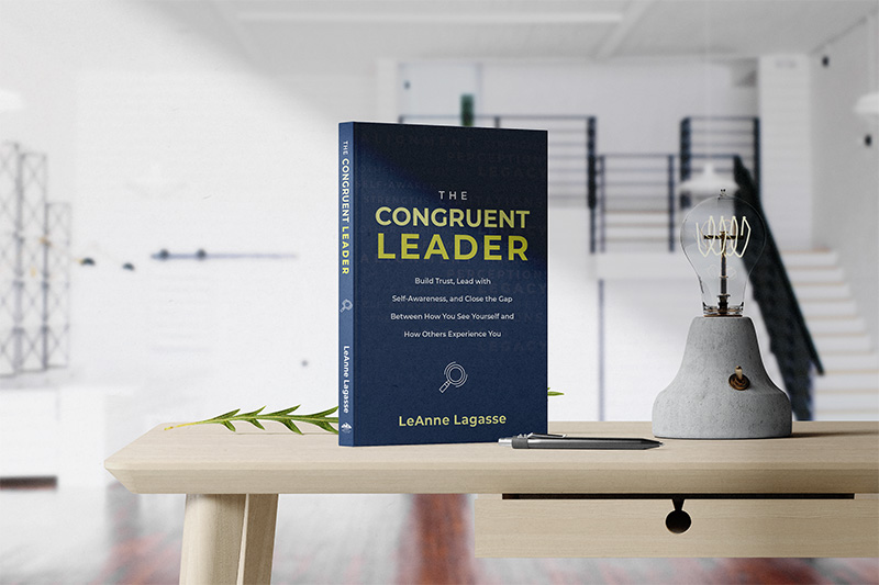 The book "The Congruent Leader: Build Trust, Lead with Self-Awareness, and Close the Gap Between How You See Yourself and How Others Experience You" by LeAnne Lagasse on a desk with a lamp and pen